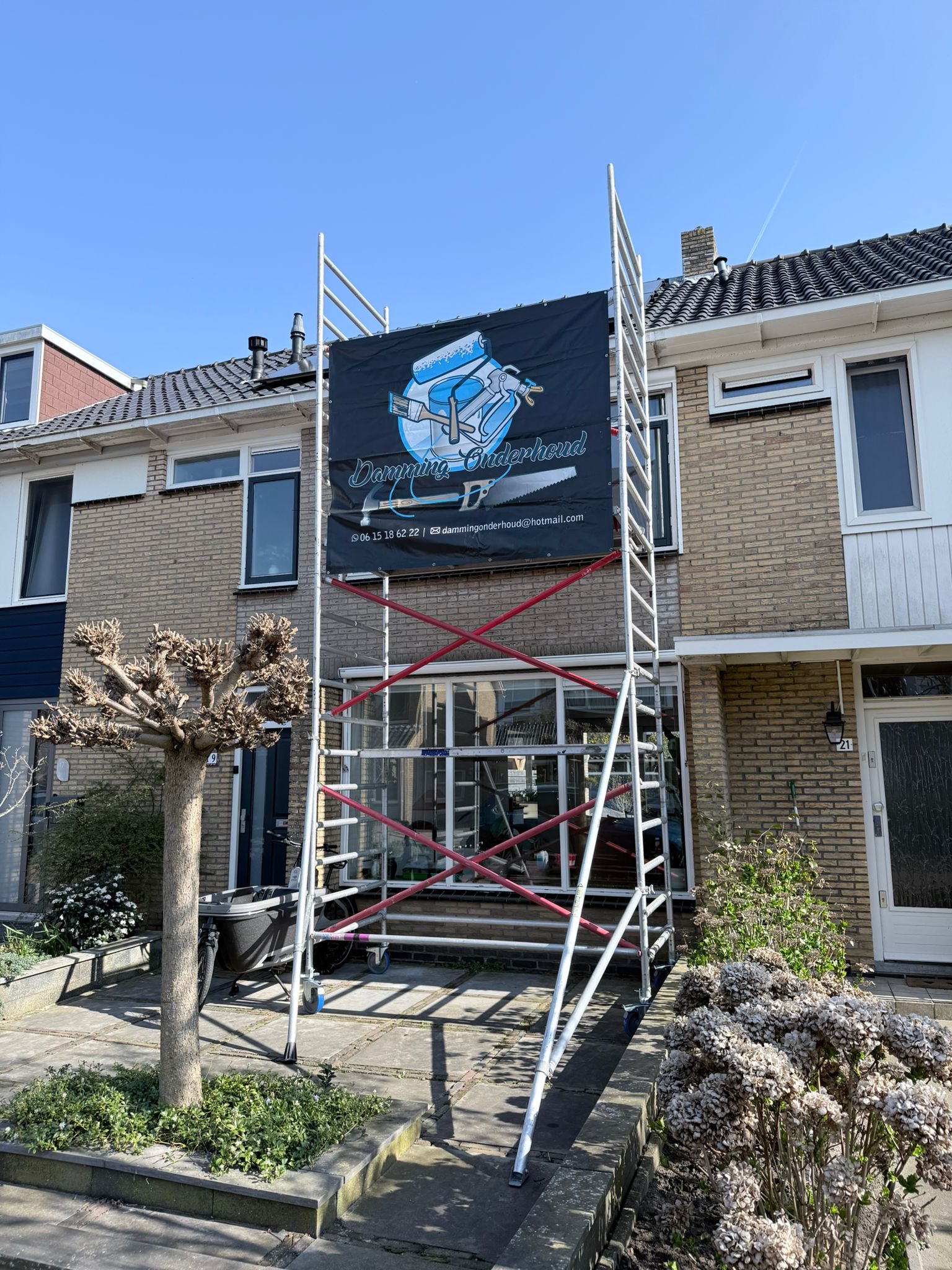 Steiger bij woning met Damming Onderhoud spandoek.