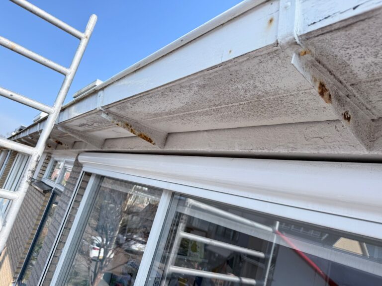 Ladder bij verweerde dakgoot aan gevel van een huis.