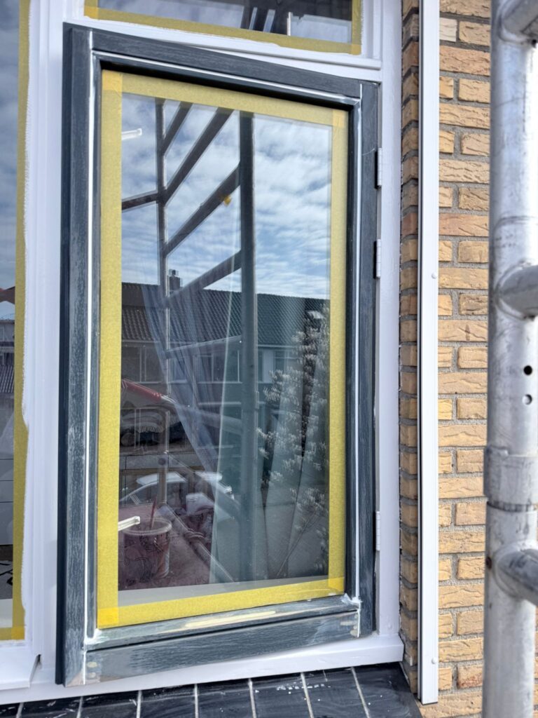 Gesloten raam met maskeringstape, klaar voor schilderwerk.