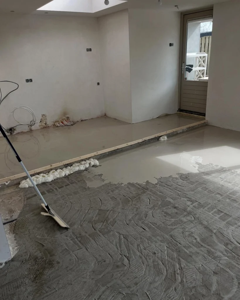 Egaline wordt met een rakel uitgesmeerd over een ruwe ondervloer in een lege kamer in Castricum