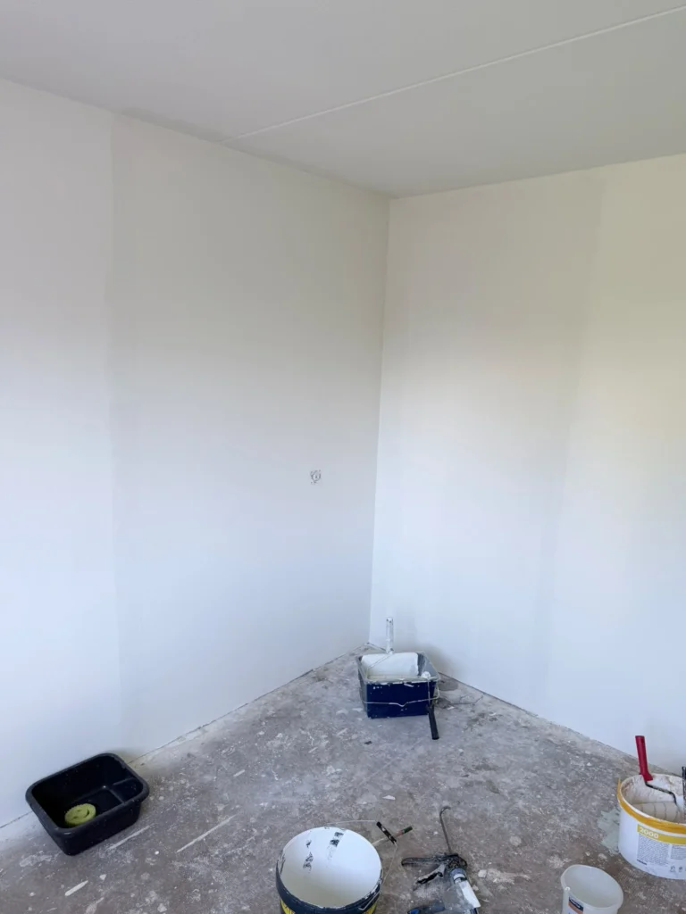 Strak witte wanden in een kamerhoek, met verfemmers en een roller op de betonvloer in Castricum