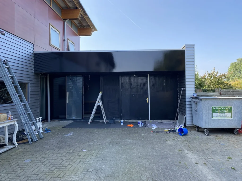 Zwart geschilderde gevelbekleding en pui van een bedrijfspand, met ladders op het terrein in Castricum