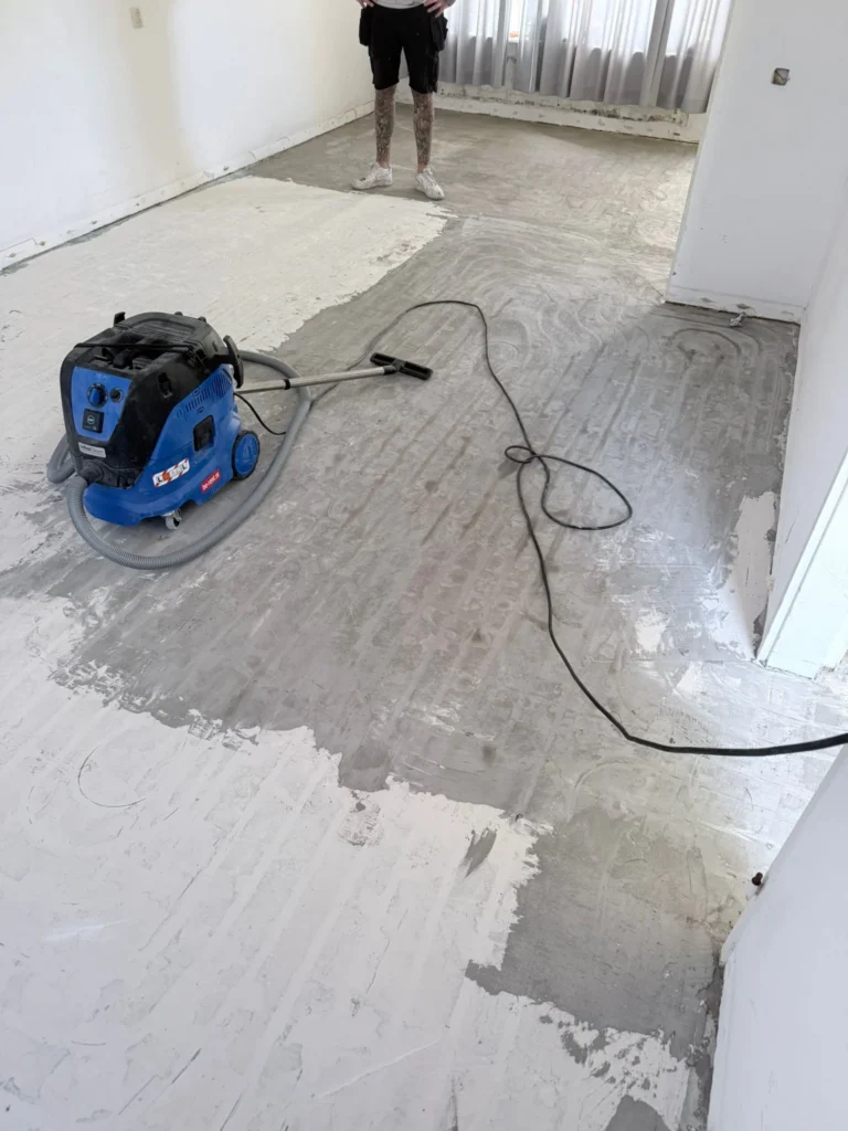 Bouwstofzuiger op een deels geschuurde ondervloer in een lege kamer in Castricum
