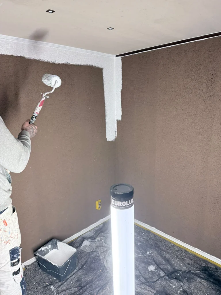Schilder rolt een bruine structuurwand wit met een verfroller in Limmen