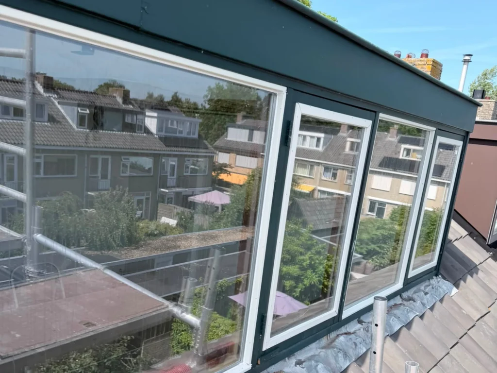 Brede donkergroene dakkapel met nieuwe beglazing in witte glaslatten op een pannendak in Uitgeest