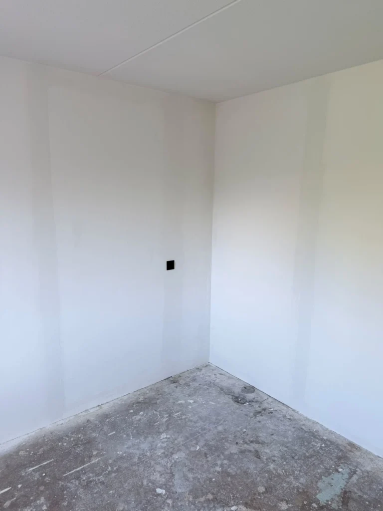 Strak witte wanden in een lege kamerhoek met kale betonvloer in Uitgeest