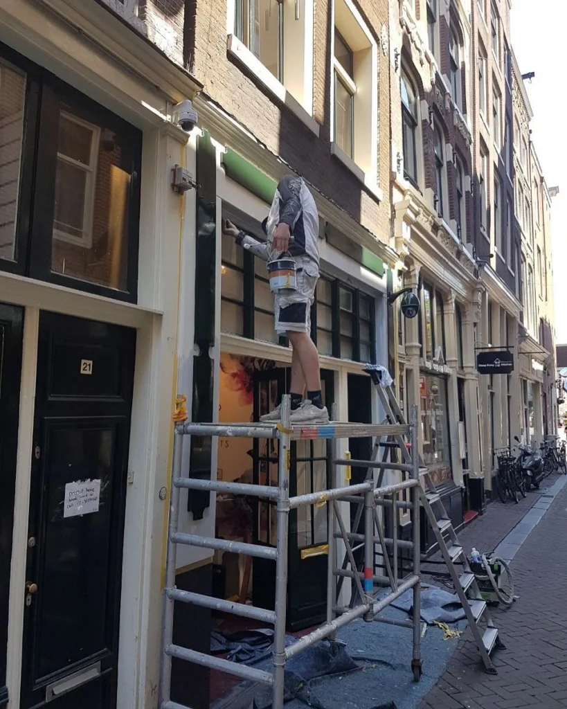 Schilder op een rolsteiger schildert de pui van een winkelpand in een smalle straat in Castricum