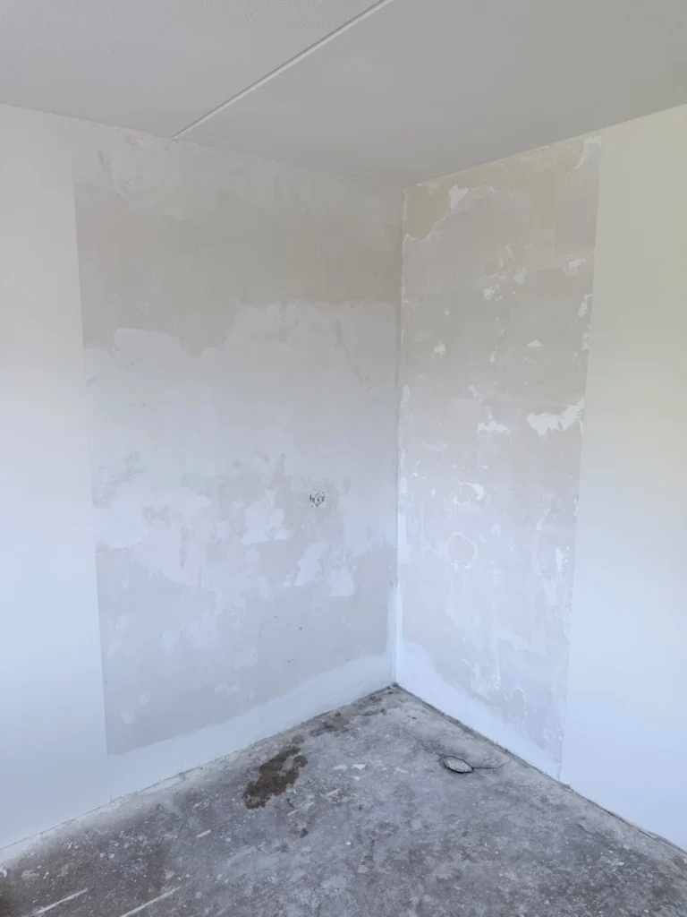 Hoek van een kamer met vlekkerig geplamuurde wanden boven een kale betonvloer in Castricum