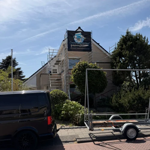 Woning in de steiger met bedrijfsspandoek, donkere bus en aanhanger ervoor in Castricum