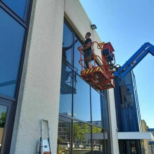 Vakman in een hoogwerker werkt aan de glasgevel van een bedrijfspand in Akersloot