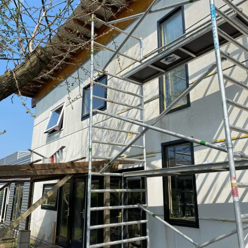 Woning met lichte gevel en zwarte kozijnen in de rolsteiger onder een houten dakoverstek in Akersloot